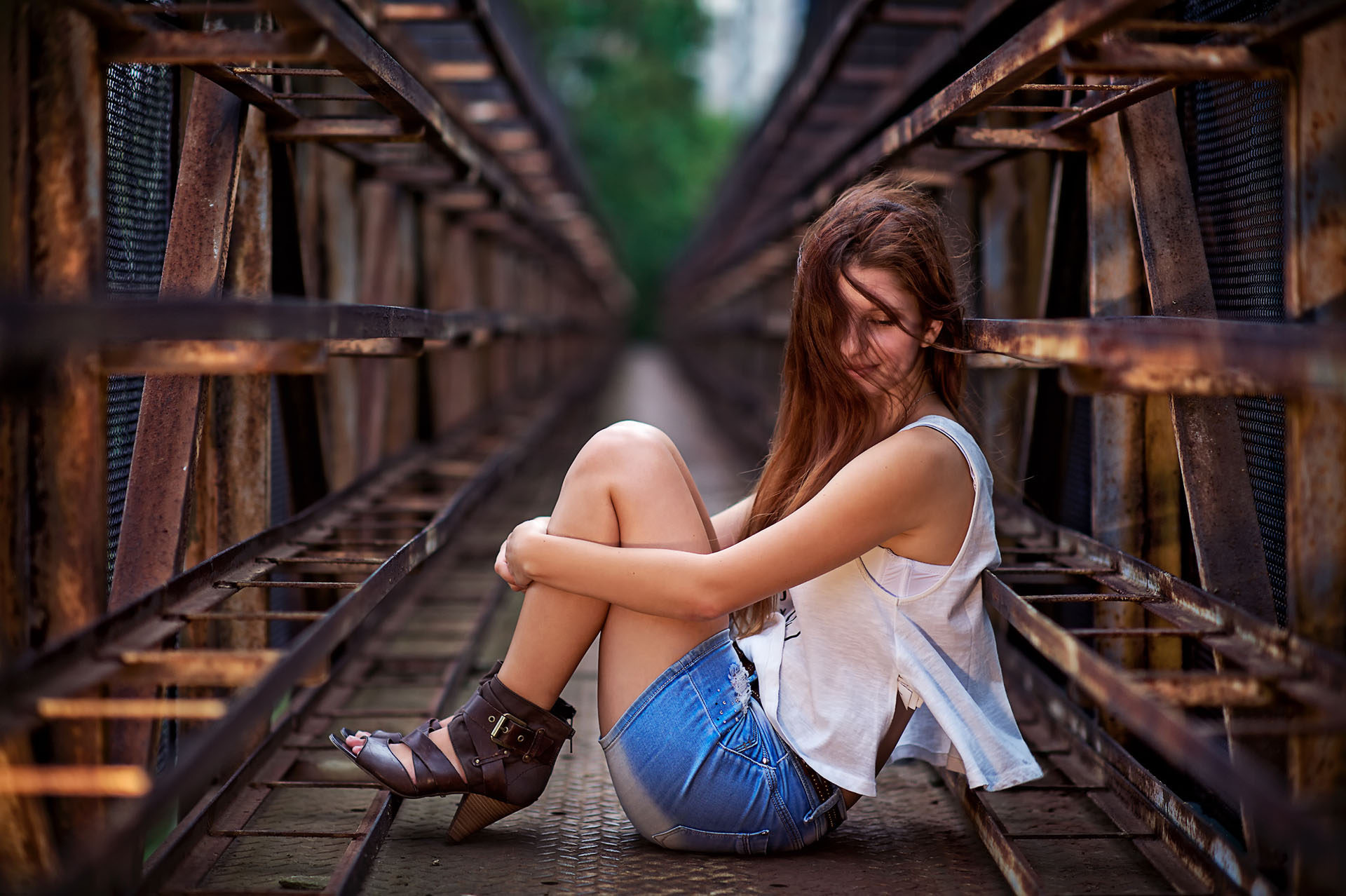 Pretty and young girl sitting on a rusty metal bridge
