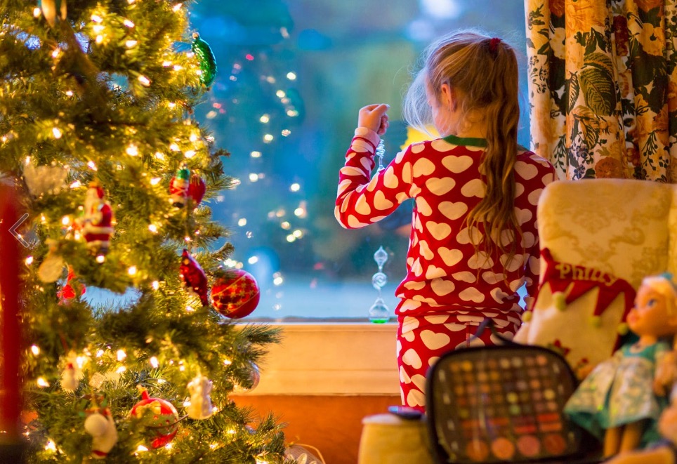 Caucasian girl looking out window near Christmas tree