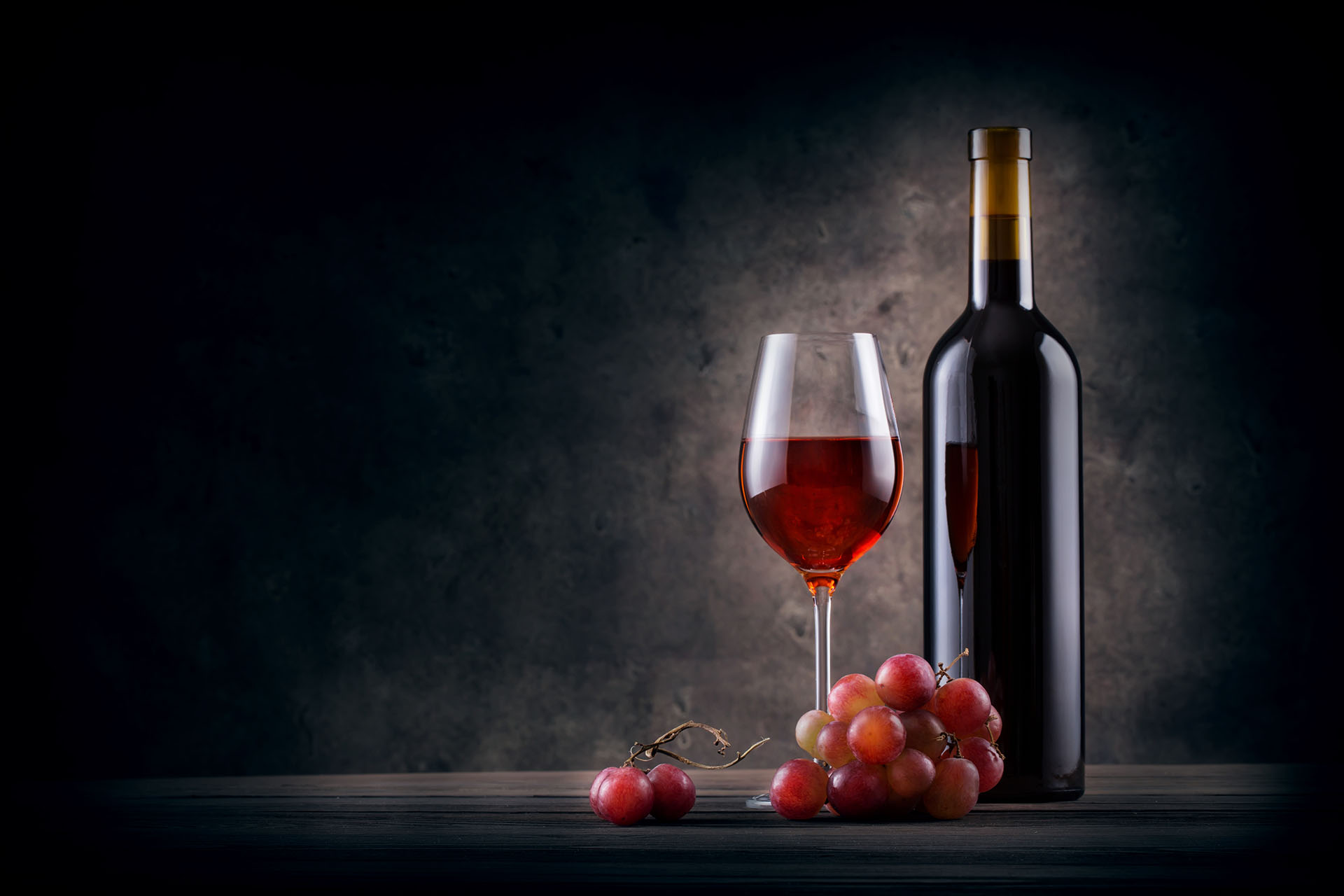 Bottle and glass of red wine with grapes on grange background