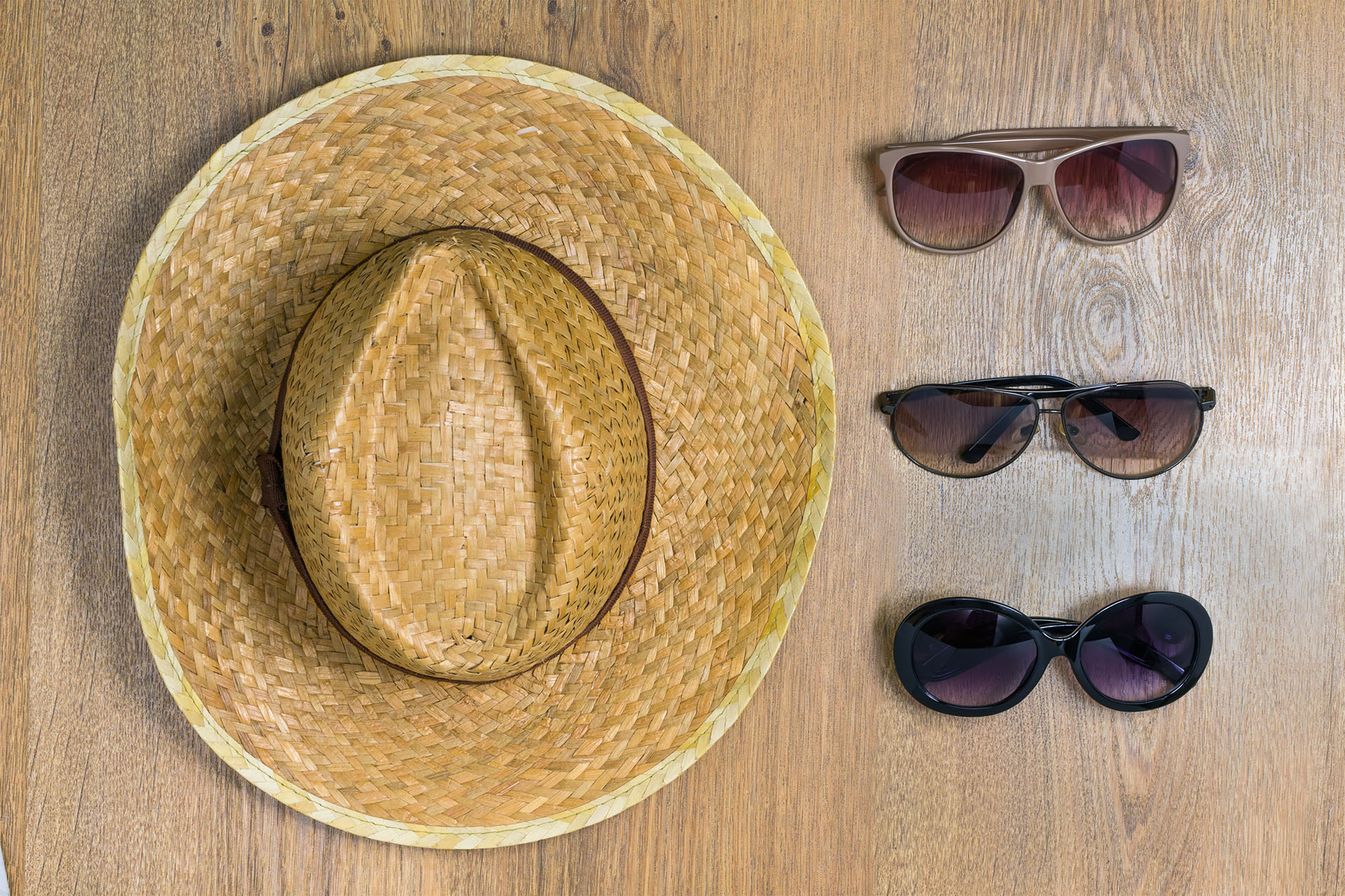 Top view of braided hat and three pair of glasses on a wooden background