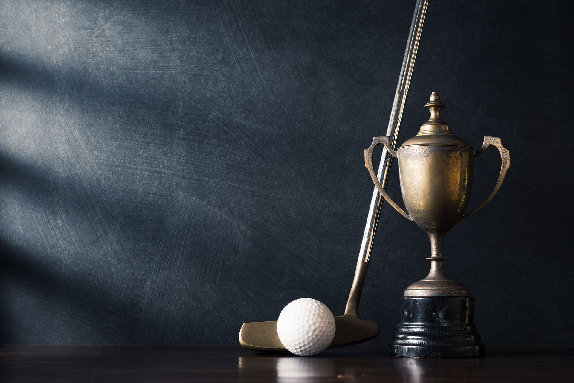 still life photography -golf club (putter) and ball with old trophy on wood table