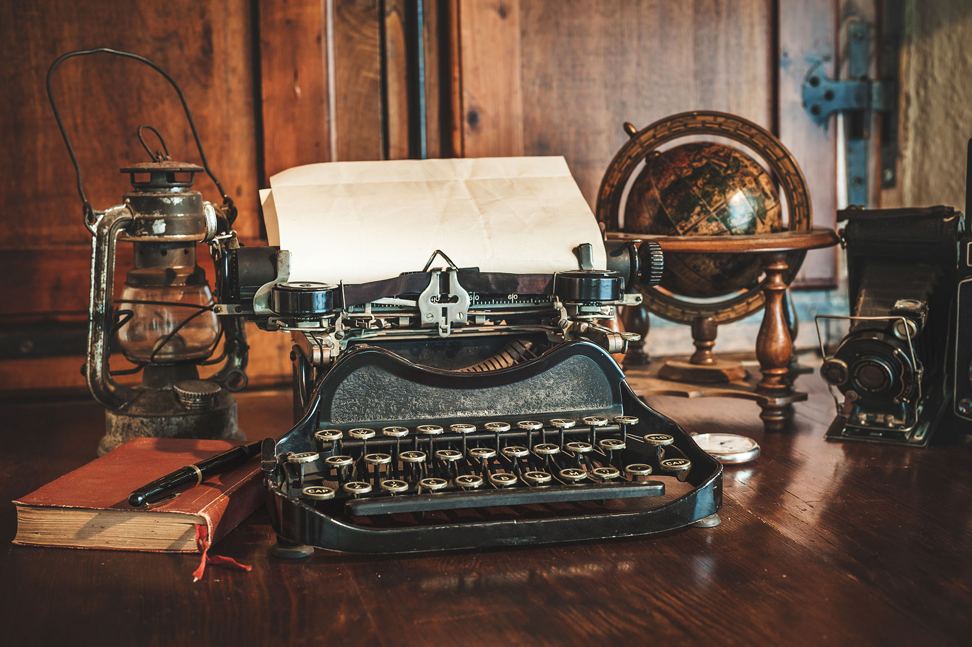 vintage photography still life with typewriter, folding camera, globe map and book on a wood table