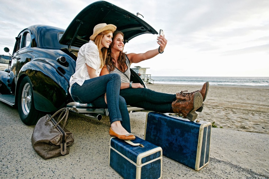 women-with-luggage-and-vintage-car-on-beach