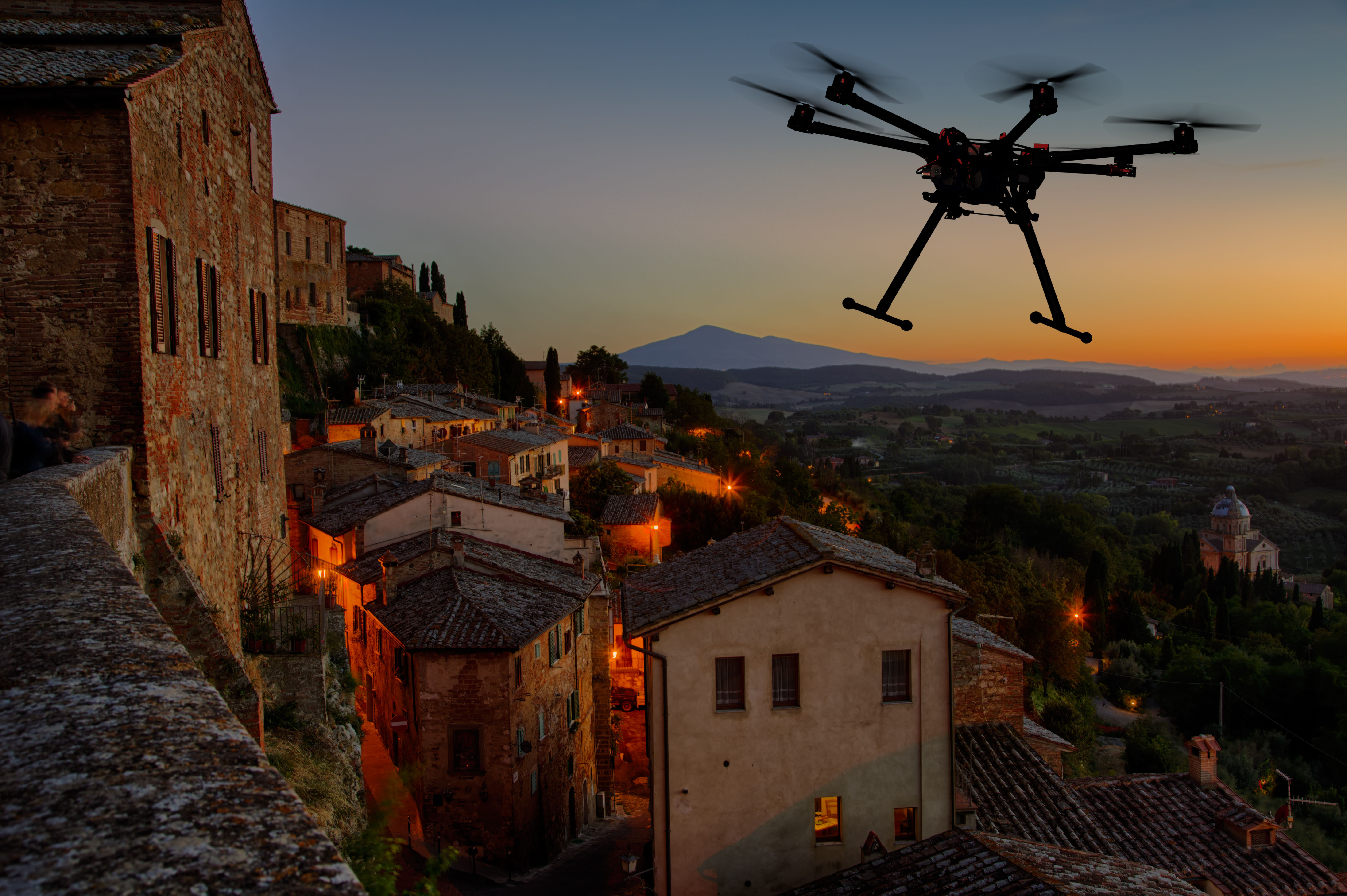 A silhouette of a flying drone with a dramatic sunset in the background in the skies of old European city