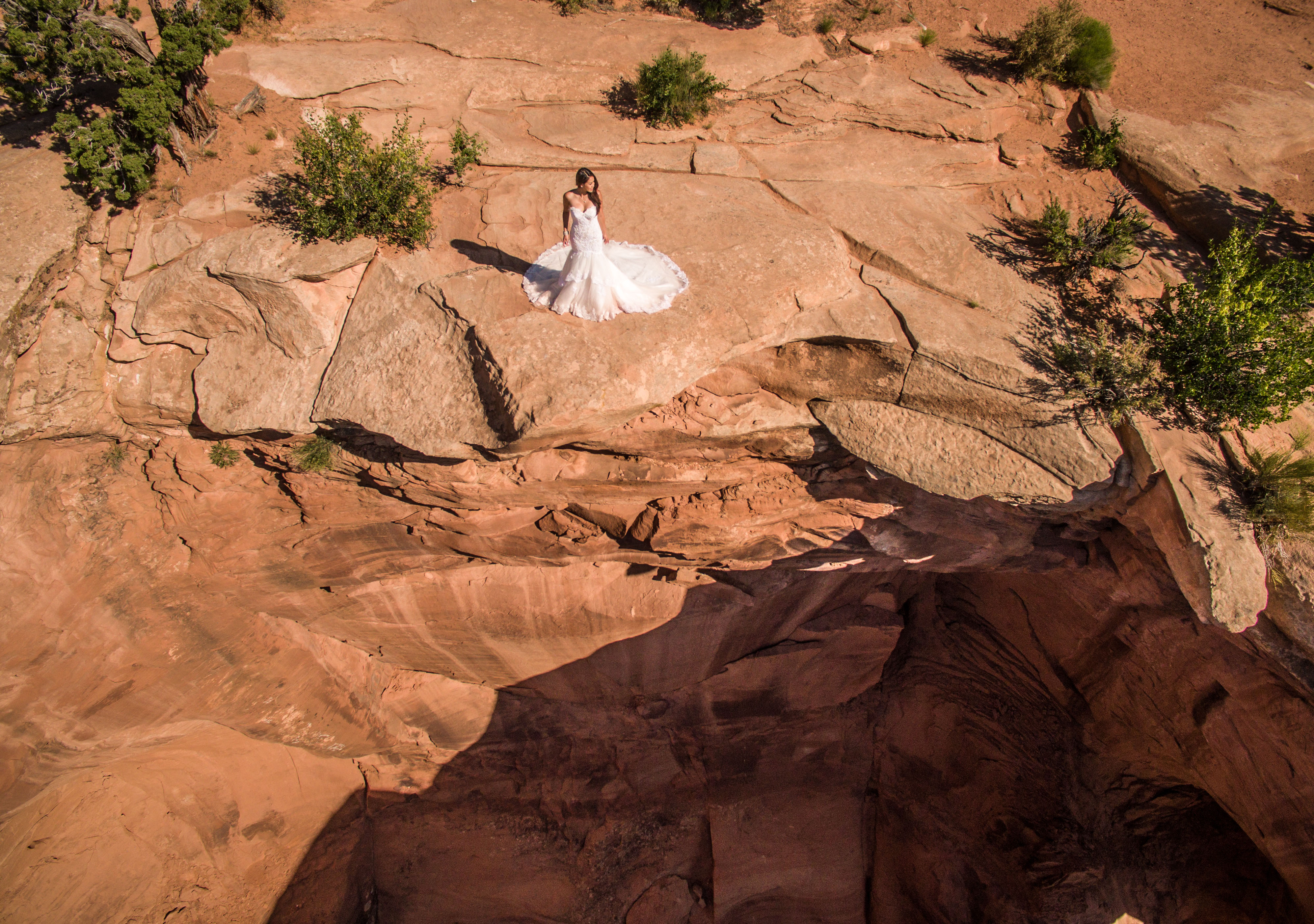 Drone photo of a Bride in her wedding dress on a cliff overlooking a massive sinkhole in the Utah Desert