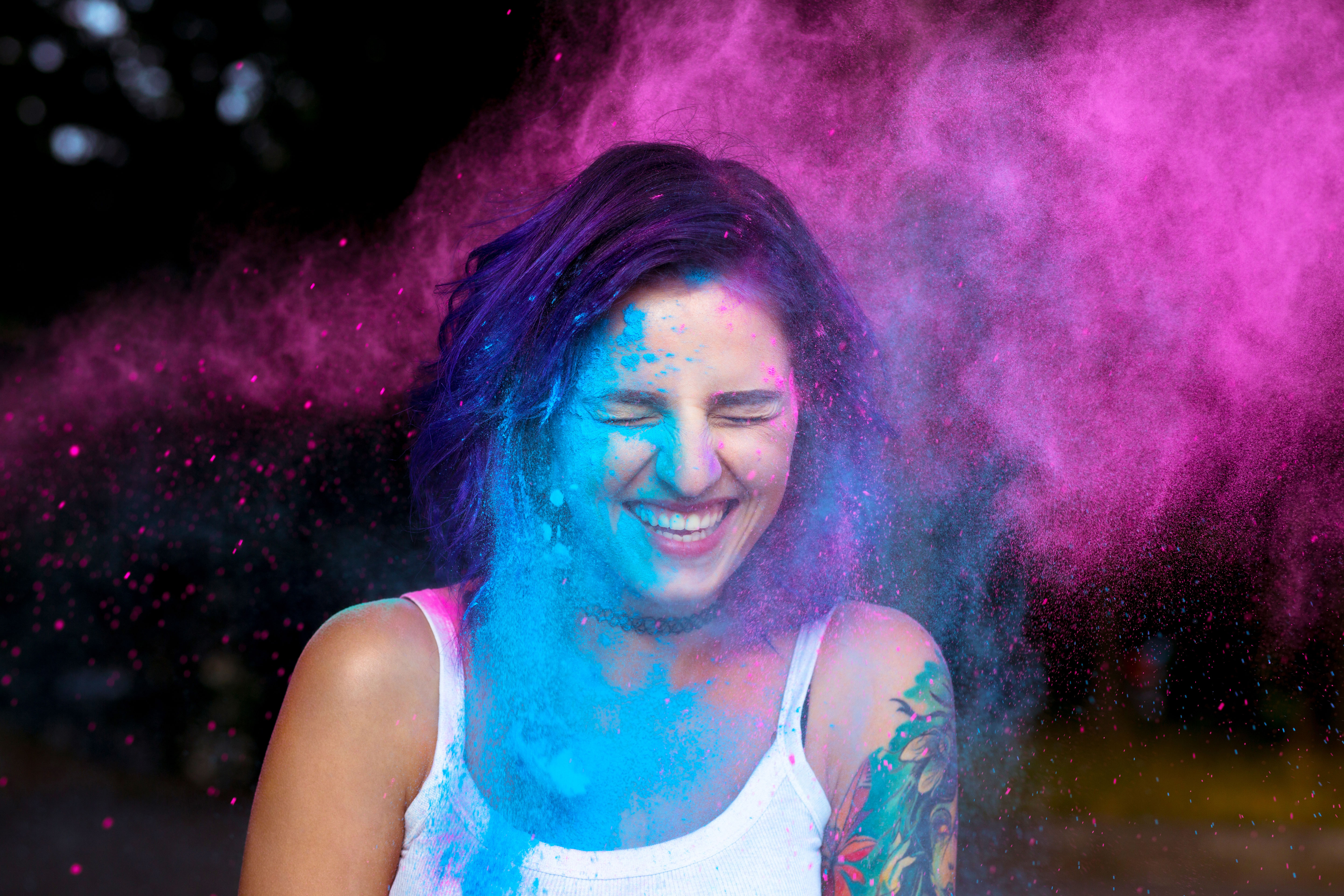 Laughing young woman with dry color powder Holi exploding around her