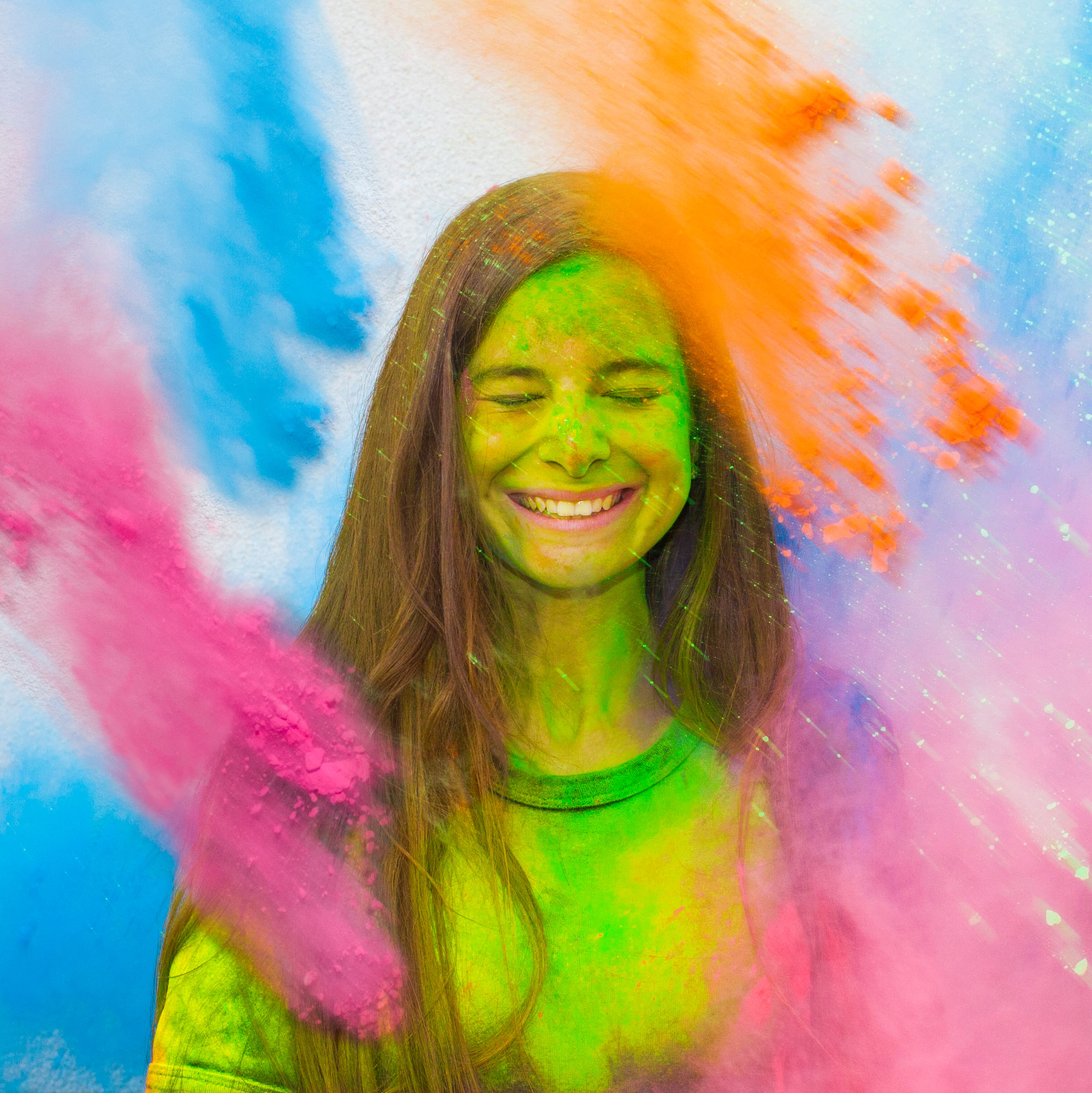 Young cheerful girl under explosion of colored powder at Holi colors party