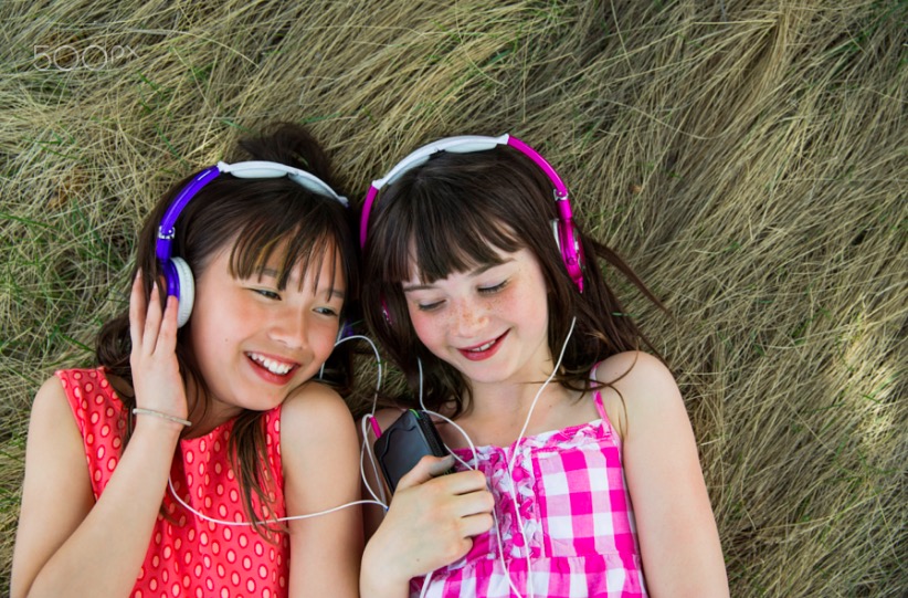Smiling girls lying on hay listening to music