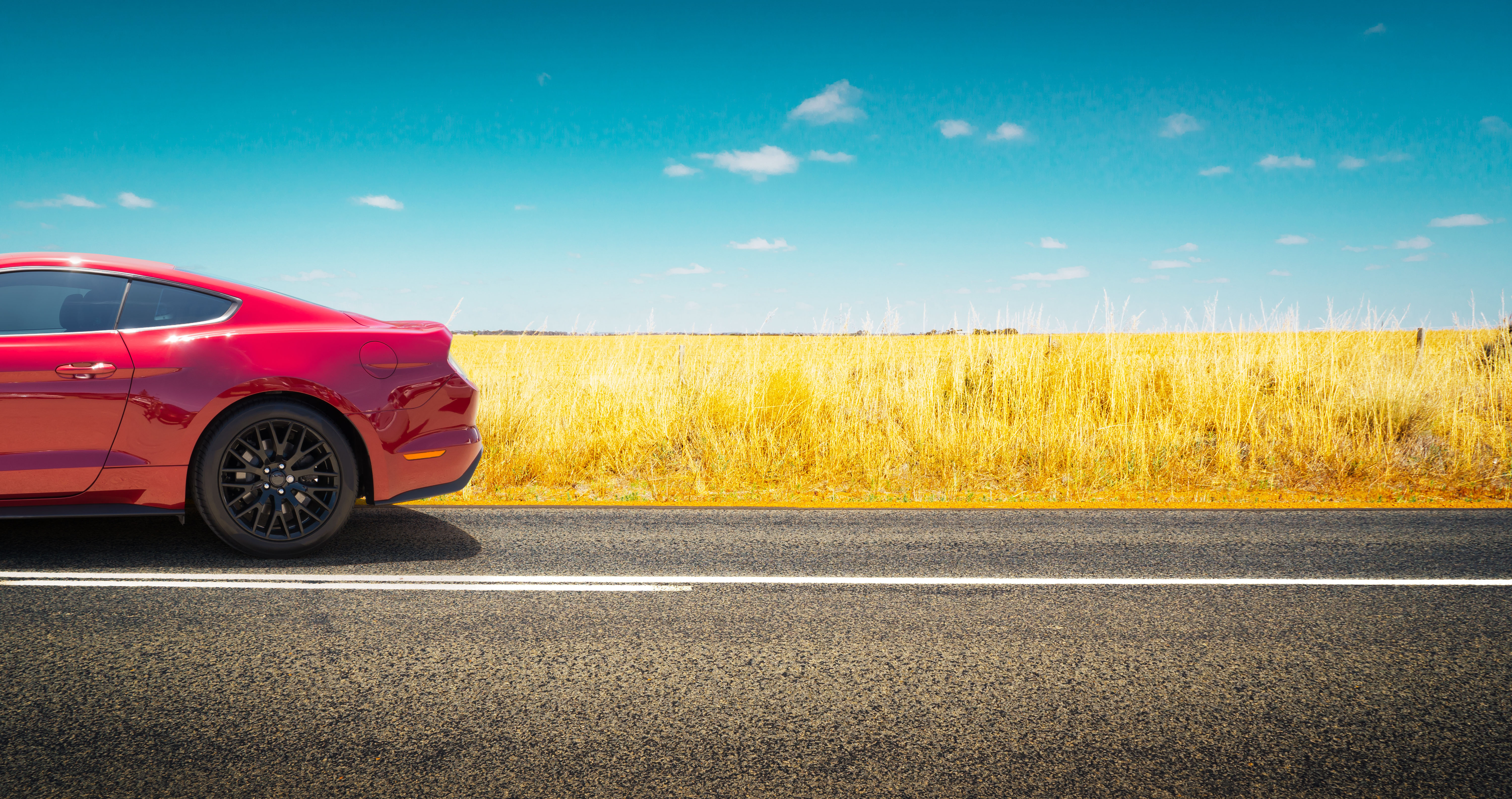 Sports car parked on road side with fields of golden wheat background