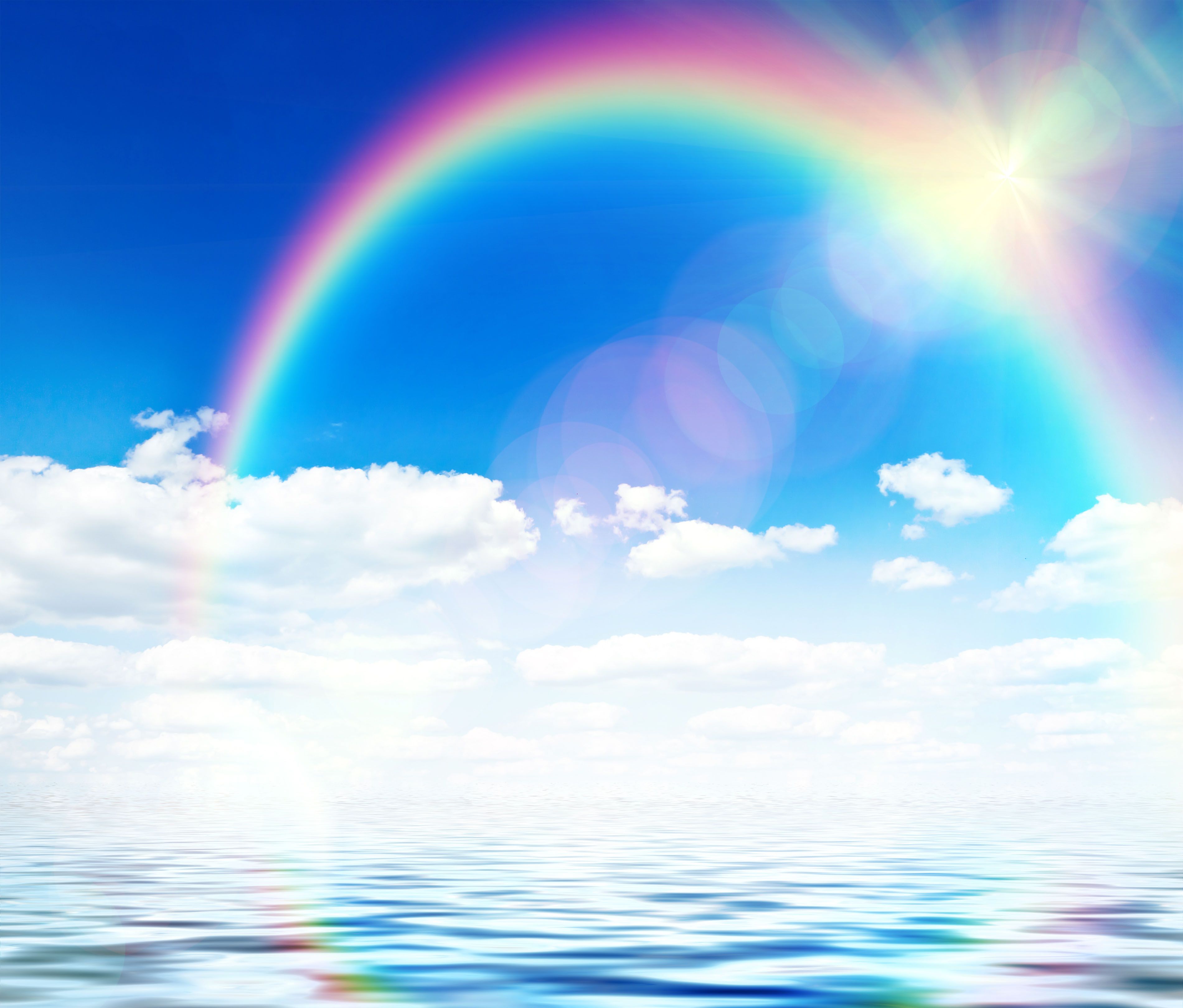 Blue sky background with rainbow and reflection in water