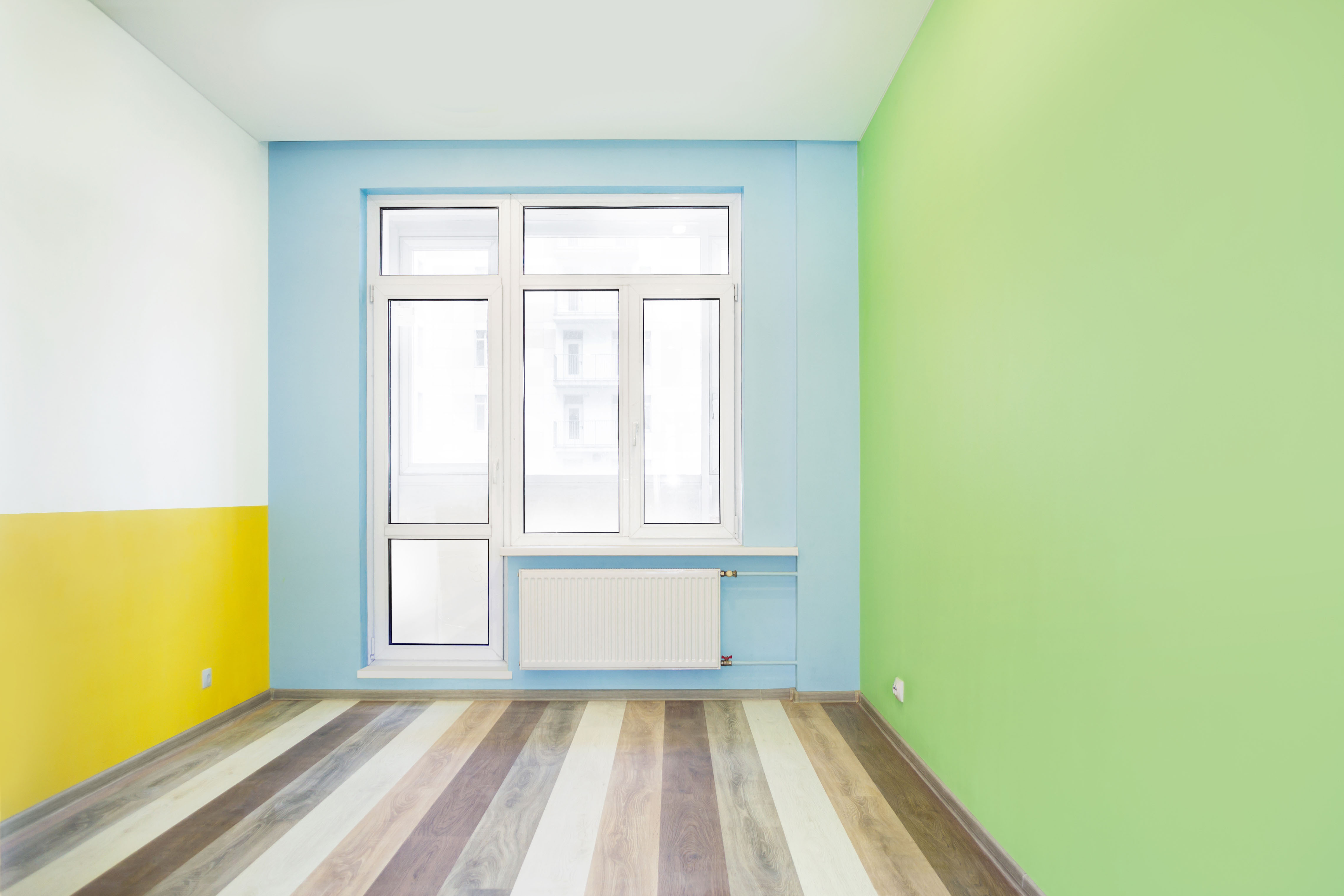 Empty cheerful kids room with green, yellow and blue color walls and wooden flooring after renovation