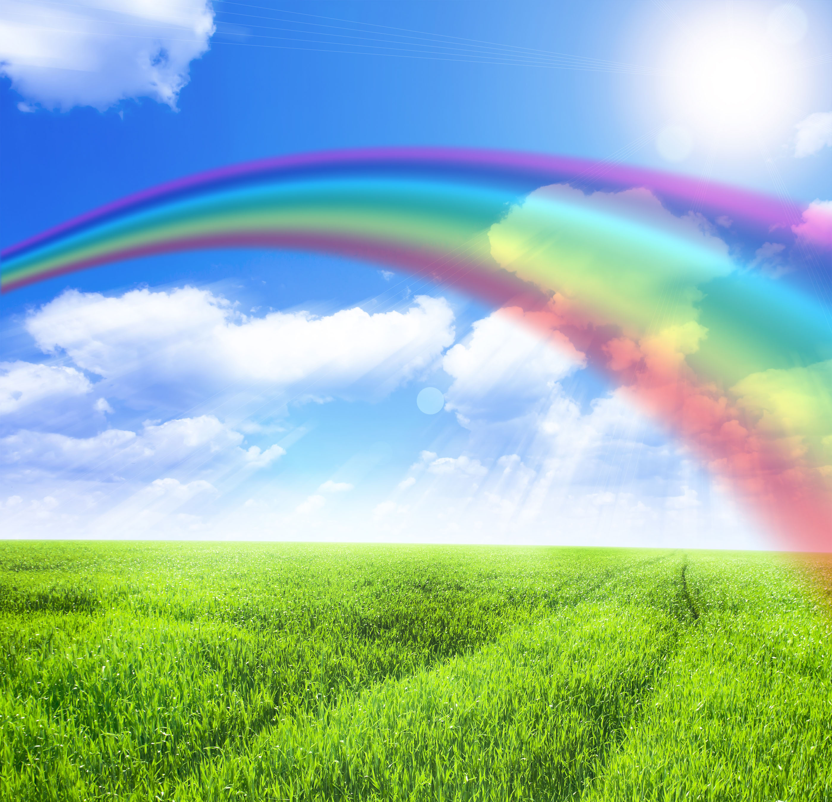 Green field under blue sky with sun and rainbow