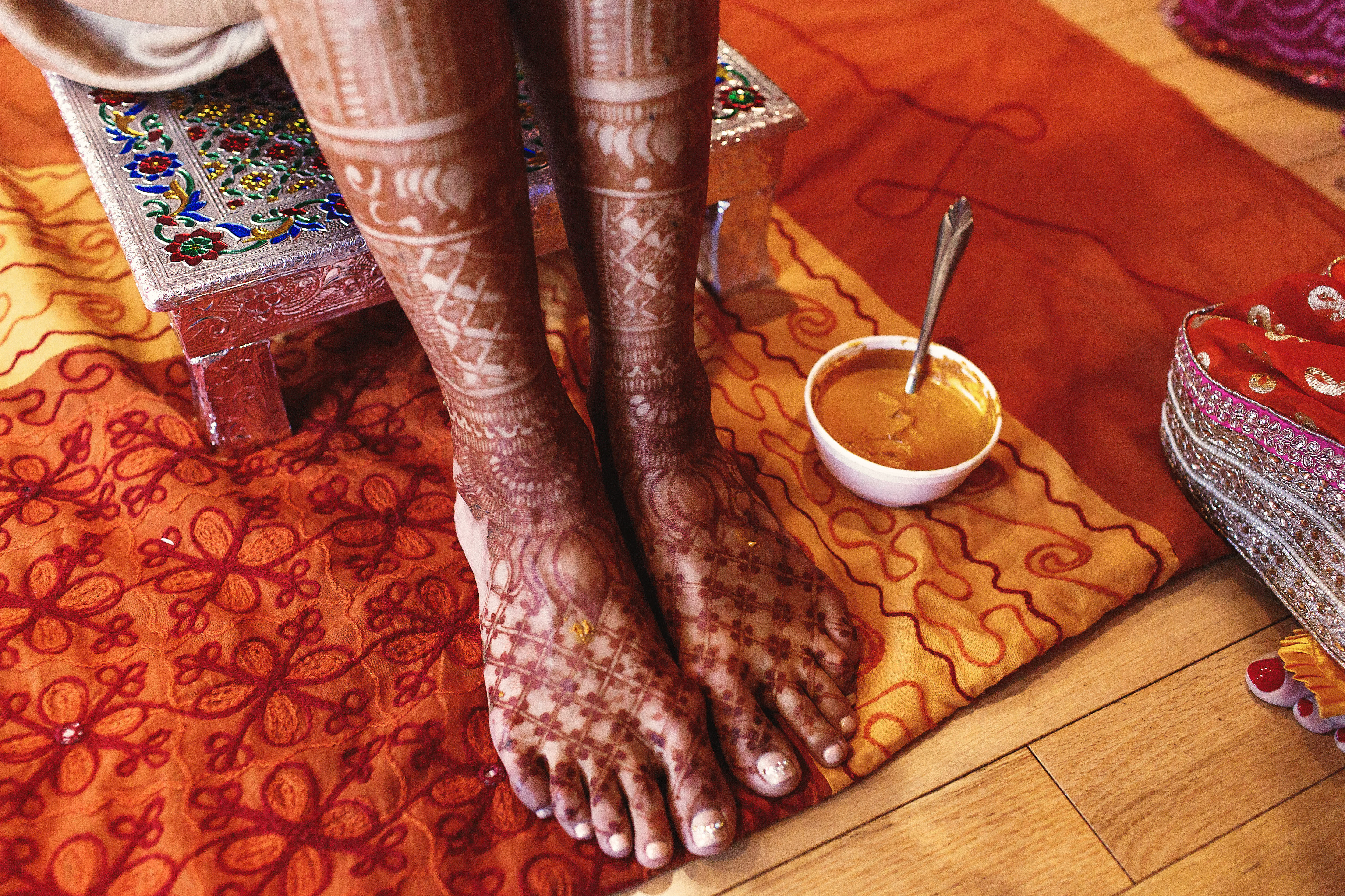 turmeric paste stands beneath Indian bride's feet covered with mehndi