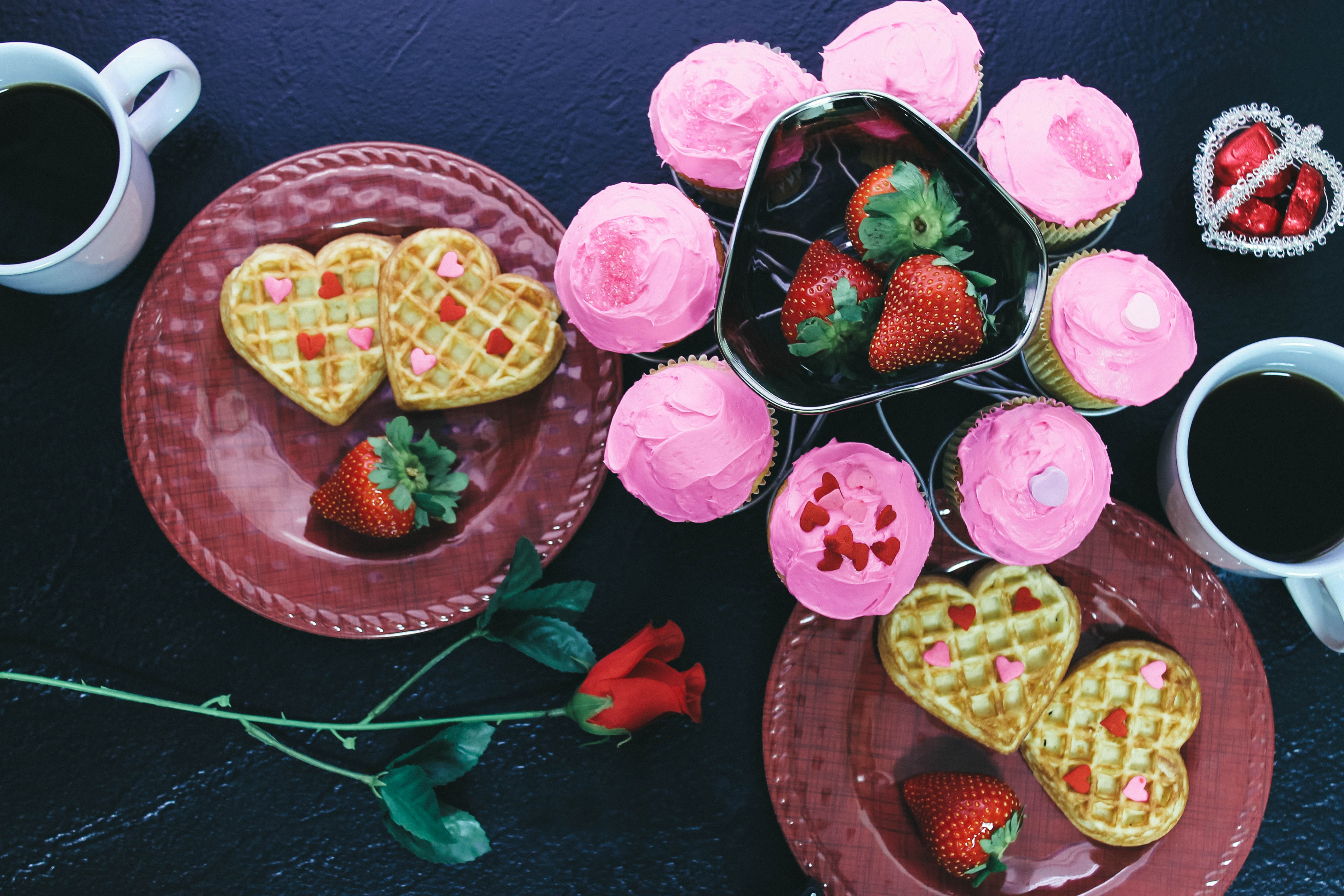 Overhead Valentine's Day breakfast of waffle hearts, chocolate, cupcakes, coffee