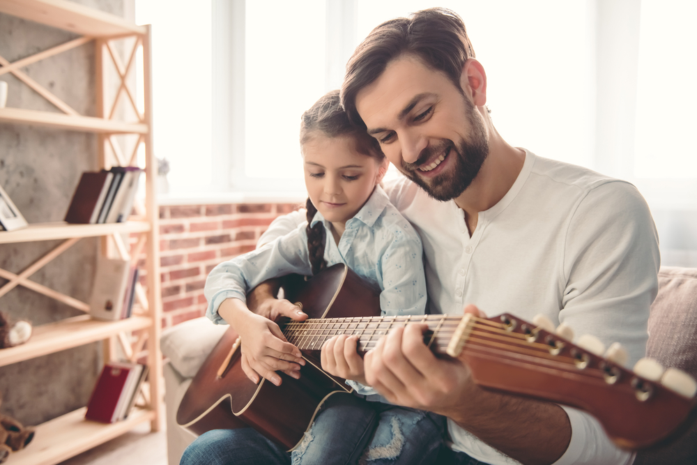 Cute little girl and her handsome father are playing guitar