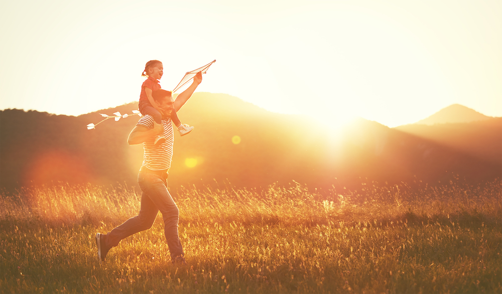 happy family father and child run on meadow with a kite in the summer on the nature