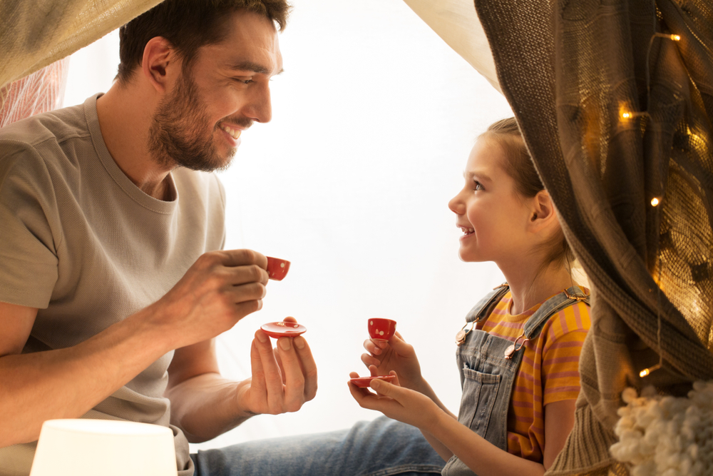 happy father and little daughter playing tea party in kids tent