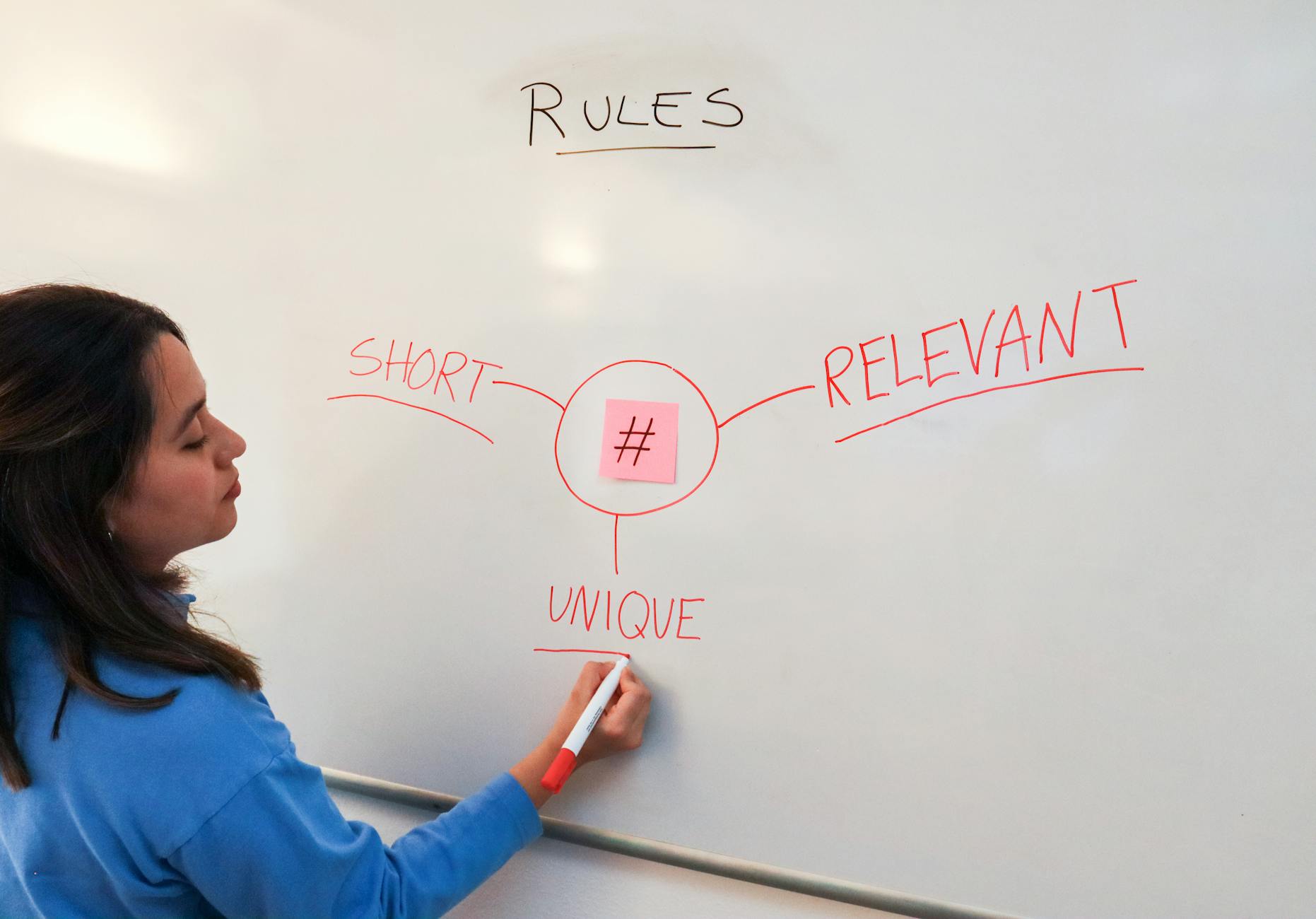 marketing specialist writing out the rules around a sticky note with a hashtag on the whiteboard